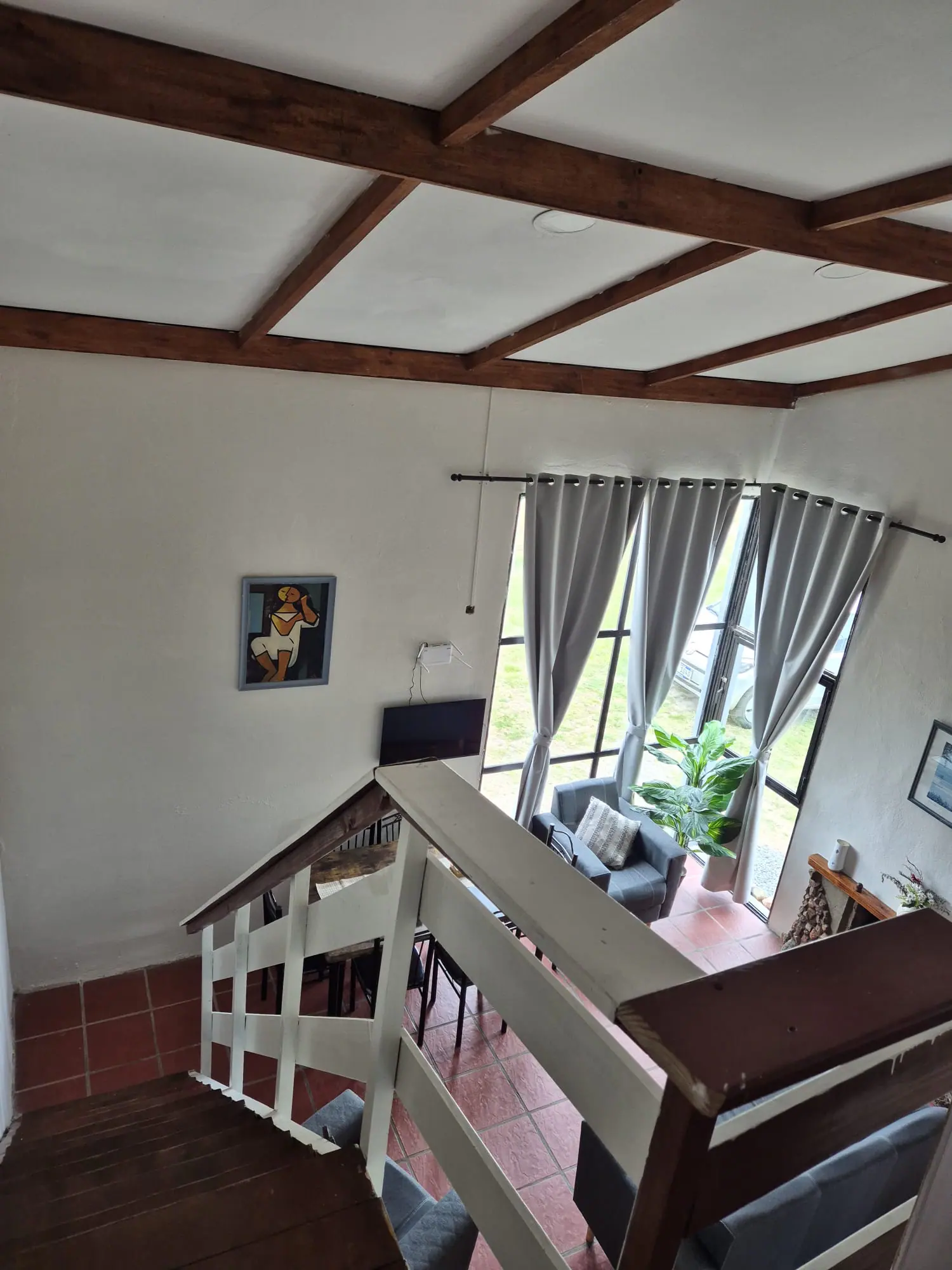 Vista desde la escalera al living de doble altura, con ventanal, butaca y estufa a leña