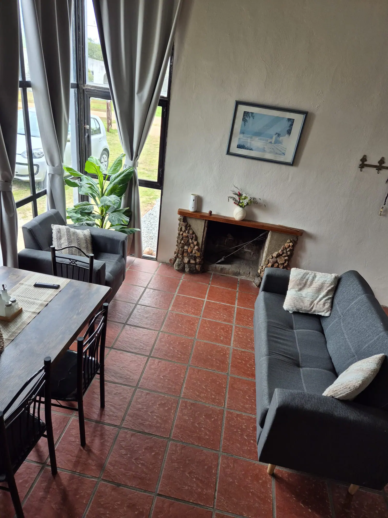 Living con sillón, butaca, estufa a leña de piedra y ventanal con cortinas