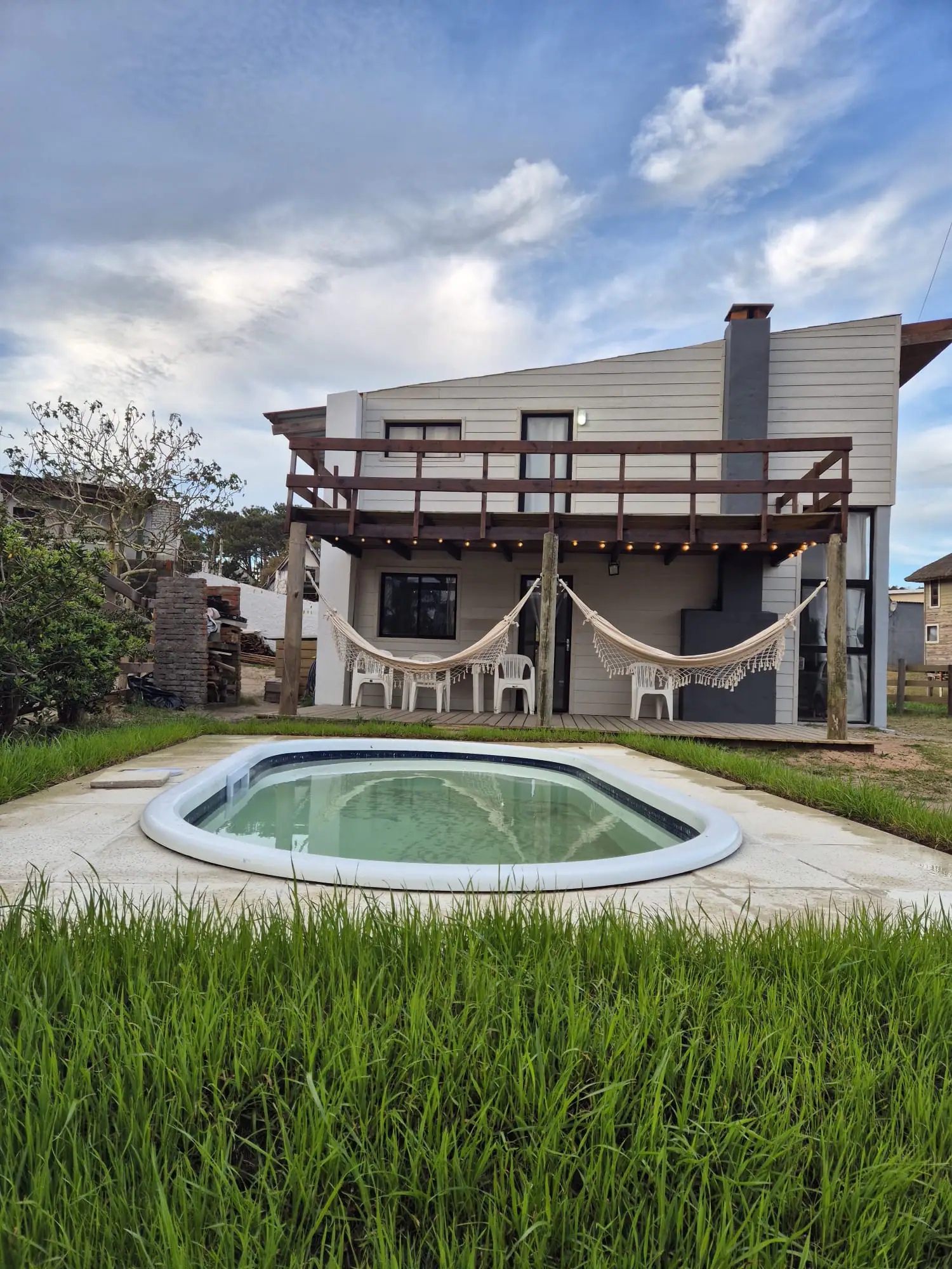 Casa de dos plantas con balcón de madera, hamacas paraguayas en el deck y la piscina en el jardín